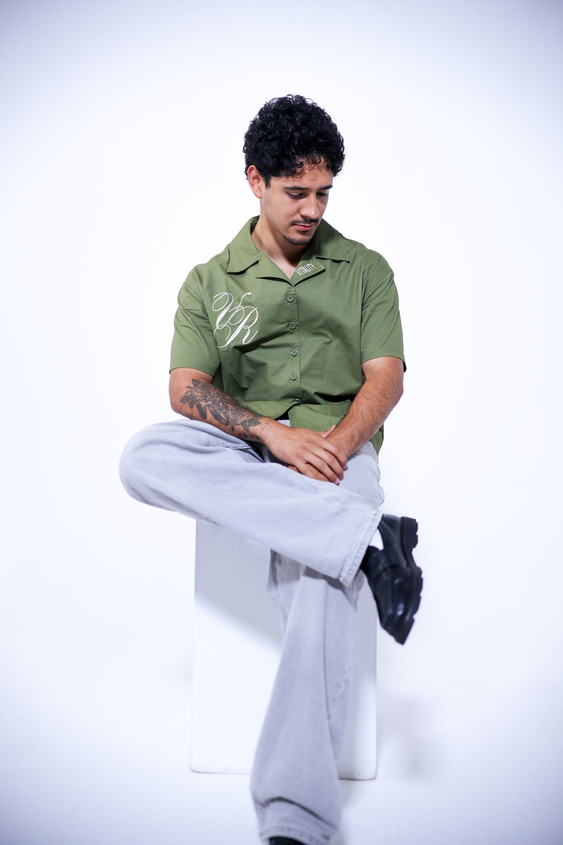 Person wearing a green shirt with a logo, sitting on a white surface.